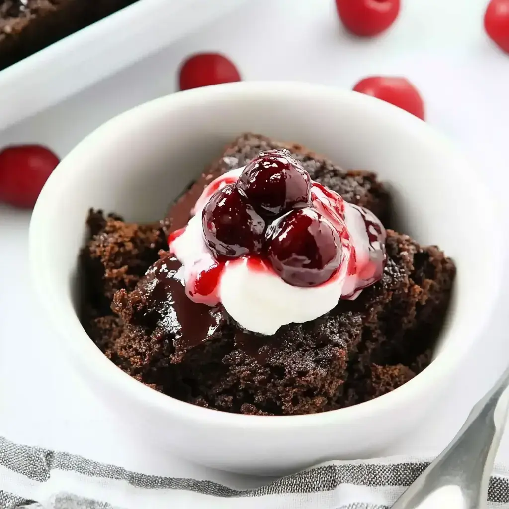 A serving of chocolate cake with cherries and whipped cream, surrounded by fresh cherries.