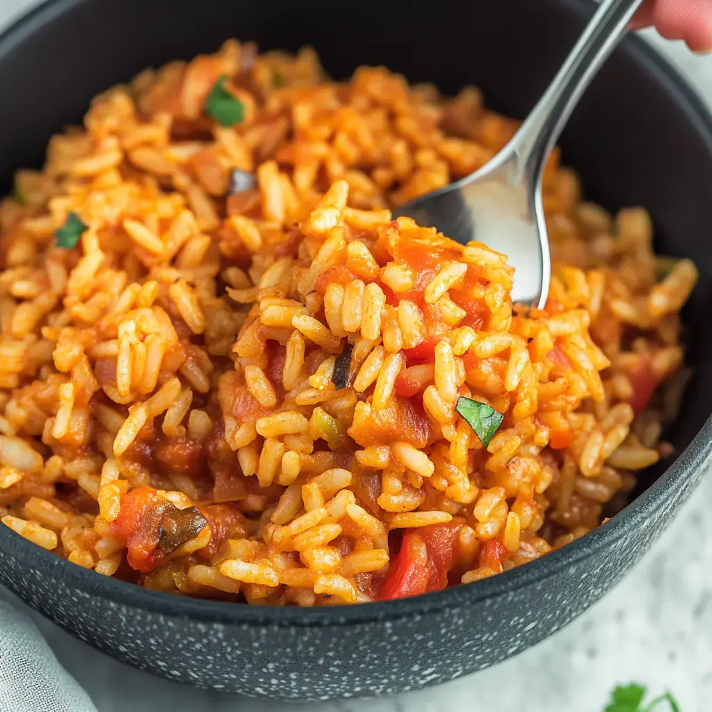 Close-up of a vibrant rice dish with tomatoes and herbs. A spoon lifts some rice from the bowl.