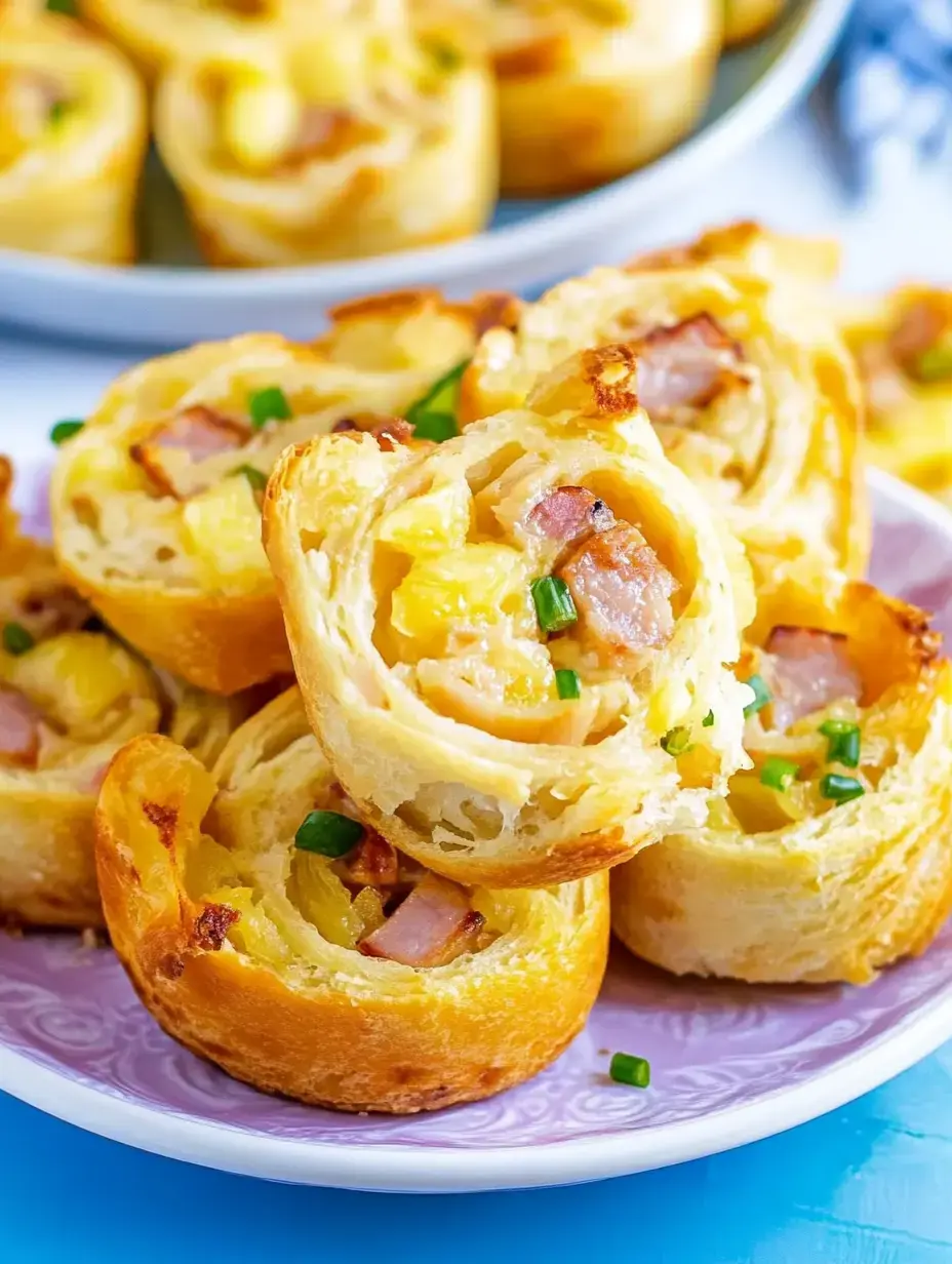 Closeup view of flaky golden pastry spirals filled with chunks of ham, pineapple bits and green onion pieces on a plate.